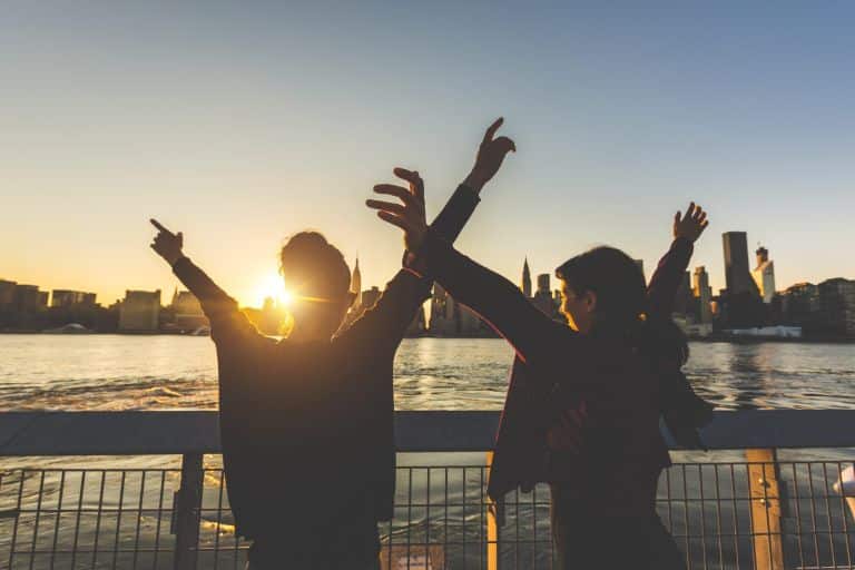 Girls with raised hands at sunset in New York. Successful and happy young women enjoying the sun setting behind skyscrapers