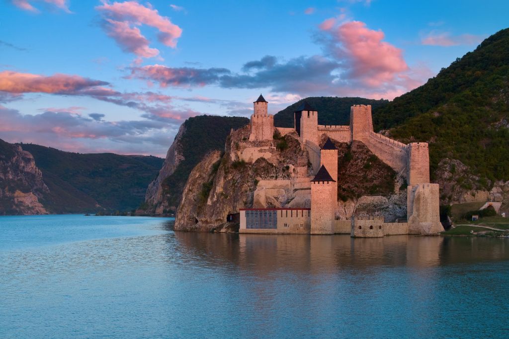 Aerial view over the water of medieval fortress Golubac illuminated by pink light of setting sun. Traveling Serbia.