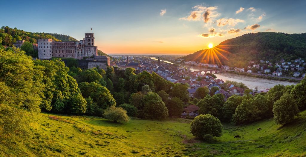 Heidelberg castle ruins on a green hill at sunrise, with the old town and river valley below.