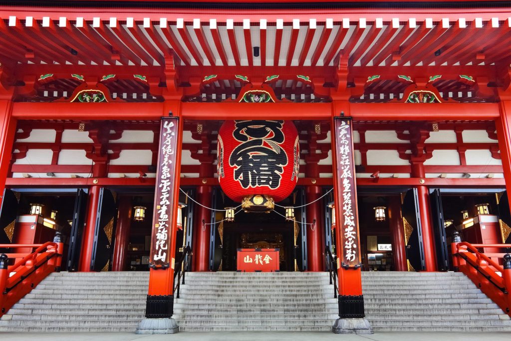 Red-and-gold temple gate with a large red lantern and steps leading up to the main hall.