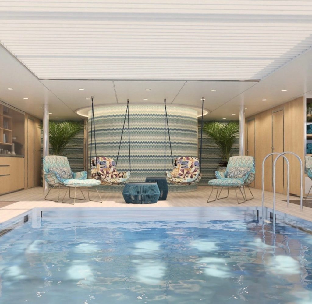 Indoor pool lounge with four hanging swings, patterned turquoise wall, and tropical chairs around a blue coffee-table, near a tiled pool edge.