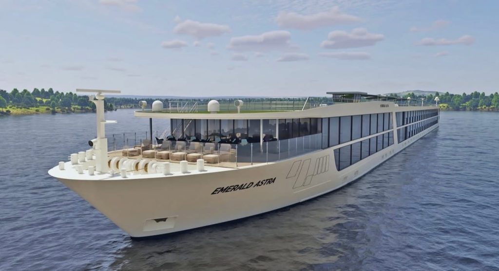 Luxurious river cruise ship Emerald Astra sailing on a calm river with a glass-walled observation deck and outdoor seating on the upper deck.