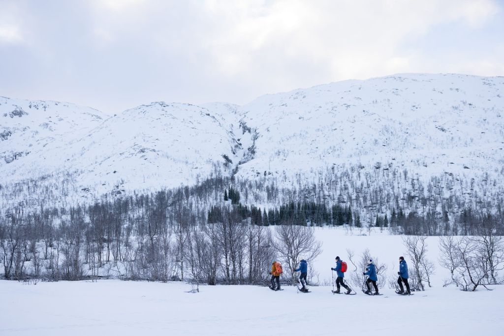 Group of snowshoers hiking across a snowy field below snow-covered hills.