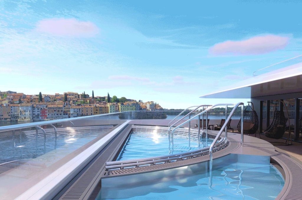 Rendered rooftop pools with glass edges overlooking a hillside town of colorful buildings.