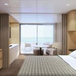Rendered suite bedroom with a sea-view balcony, round table and sofa beyond sliding doors.