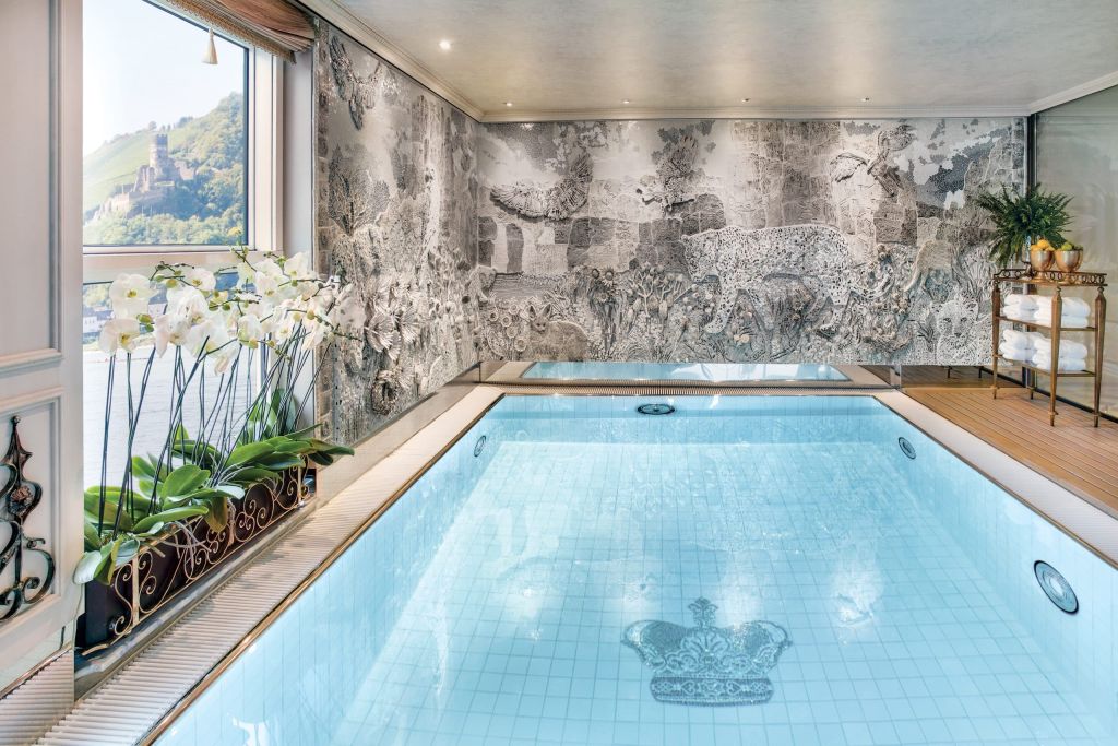 Indoor spa pool with a decorative grayscale mosaic wall, orchids by the window, and a fruit-topped towel cart nearby