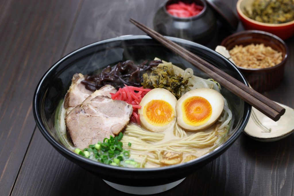Bowl of tonkotsu ramen topped with chashu pork, marinated eggs, nori, green onions and pickles.
