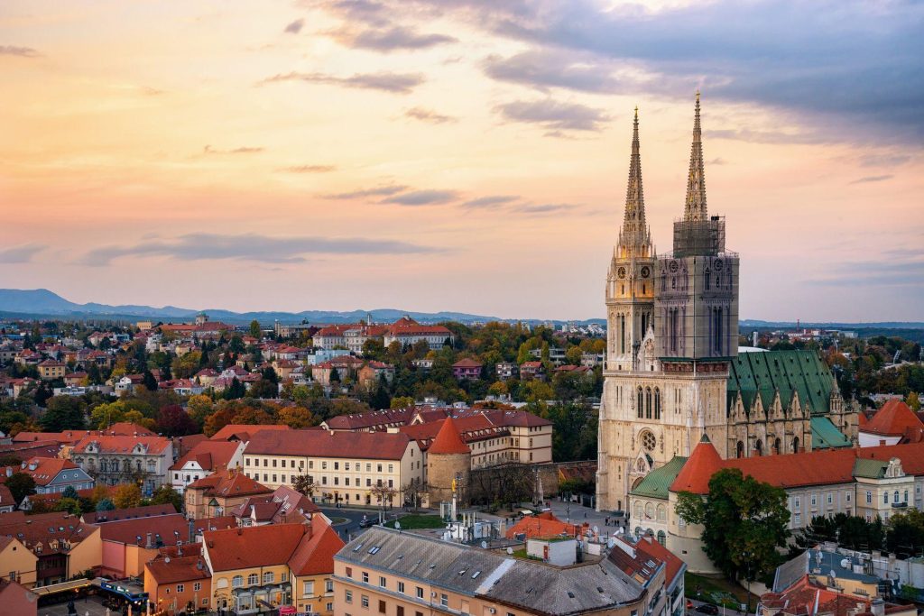 Zagreb cathedral with twin spires and a red-roofed city at sunset.