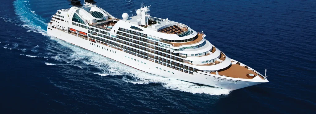 White luxury expedition ship cruising across dark blue sea with a white wake behind it.