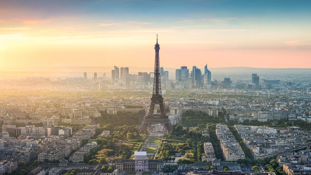 Eiffel Tower rising above a hazy city skyline at sunrise.