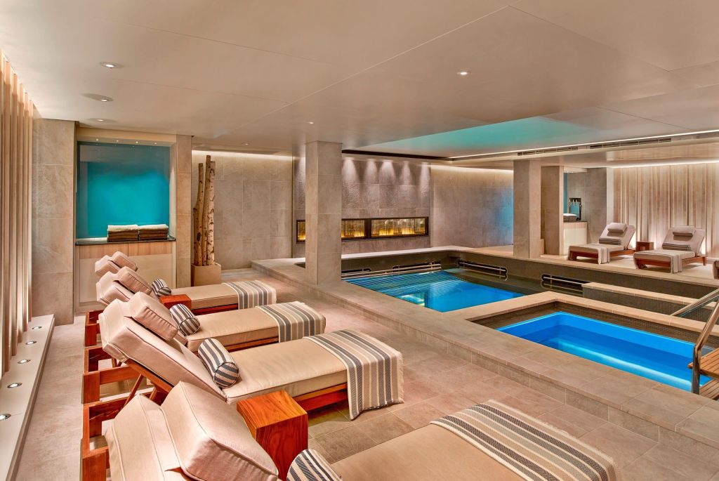Indoor spa with heated pools, loungers and a fireplace along a stone wall.