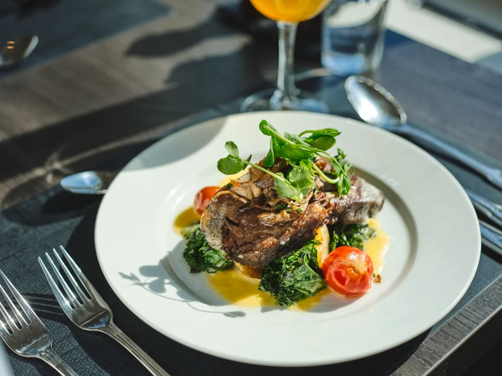 Plated dish of meat with mushrooms, cherry tomatoes, and microgreens on a white plate.