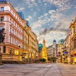 Wide pedestrian street lined with ornate historic facades, statues, and street lamps at dusk.
