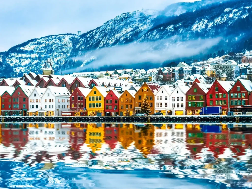 Colorful wooden waterfront houses in red, yellow and white beside a harbor with snowy mountains.