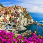 Colorful cliffside village of pastel houses on a rocky headland above a turquoise sea with a boat.
