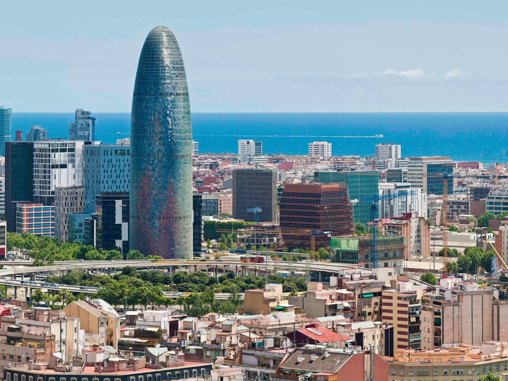 Tall curved glass tower rising above a dense city skyline with the sea on the horizon.