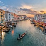 Gondola on a wide canal lined with pastel palazzo facades at sunset.