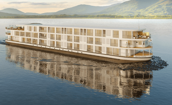 White river cruise ship with glass-walled balconies sailing on a calm river below green hills.