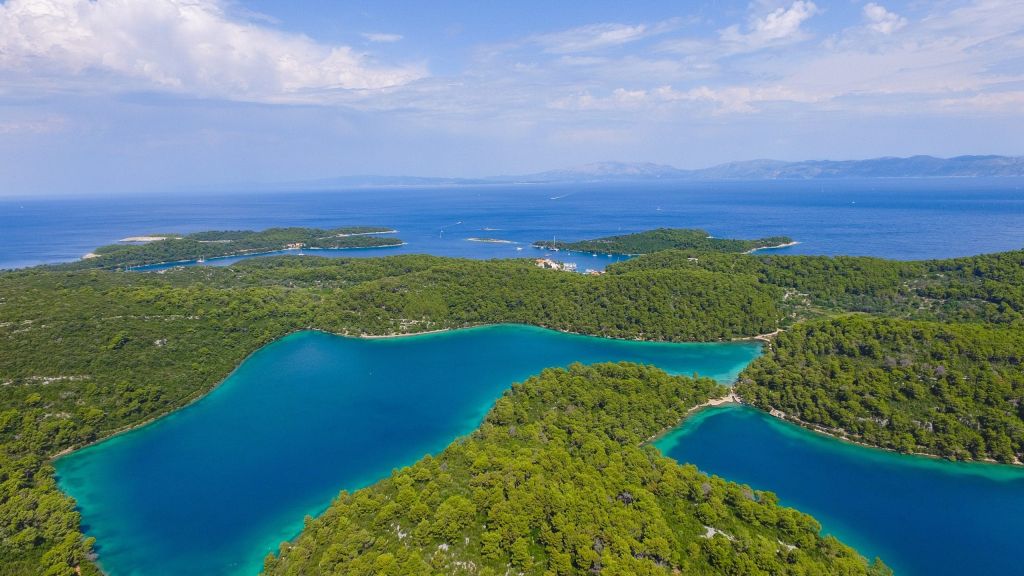 Aerial view of forested islands framing turquoise bays under a blue sky.