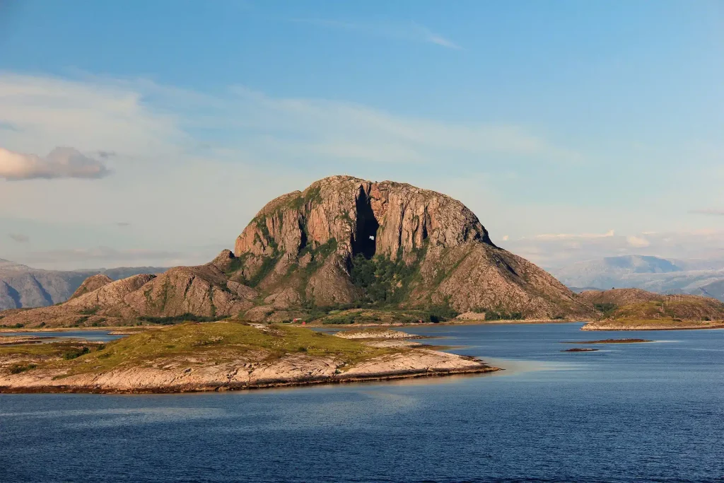 Rocky mountain with a hole through its summit rising above coastal islands under a blue sky.