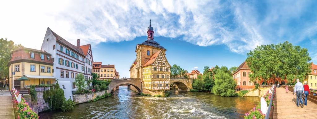 Half-timbered building on a river island with arched stone bridges and a wooden footbridge.