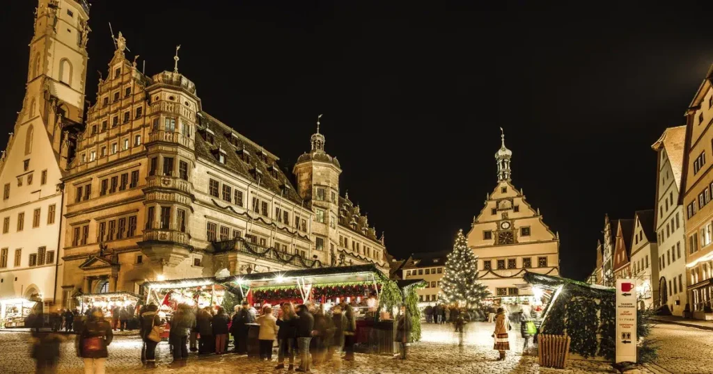 Christmas market in a medieval town square at night, with a lit tree and market stalls.
