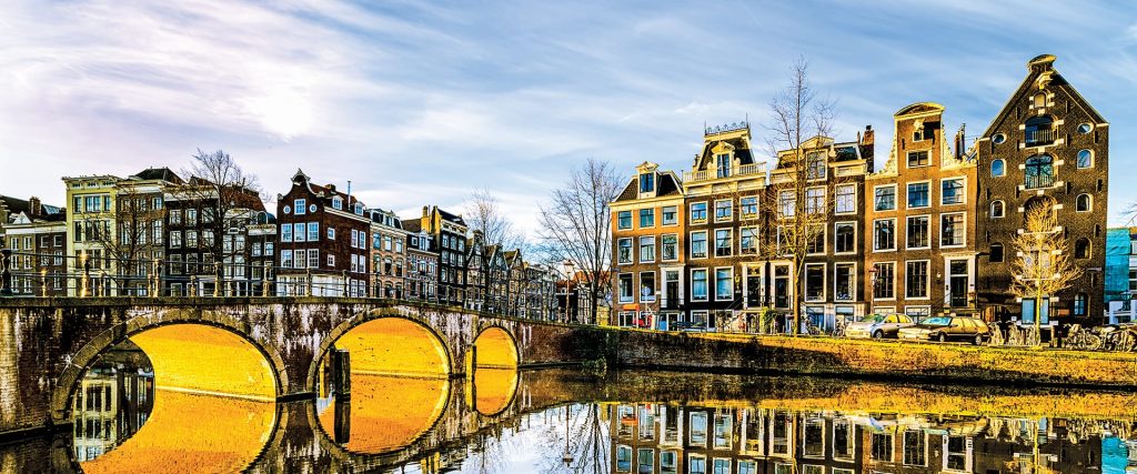 Canal with arched stone bridges reflecting golden light, lined by narrow gabled canal houses.