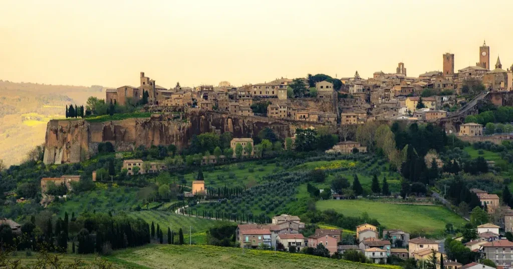 Hilltop medieval Italian town on a cliff above green valleys and cypress trees.