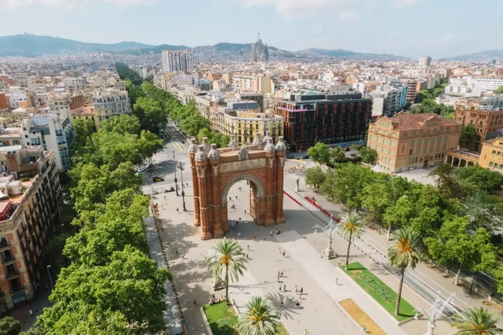 Aerial view of the red-brick Arc de Triomf on a tree-lined boulevard in Barcelona.