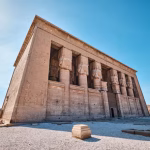 Sandstone temple facade with carved columns and statues under a clear blue sky.