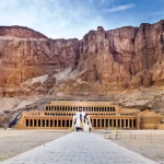Terraced temple of stone columns built into a towering cliff face, with a long paved approach.