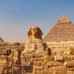 Great Sphinx in front of a large pyramid and a smaller pyramid under a hazy sky.