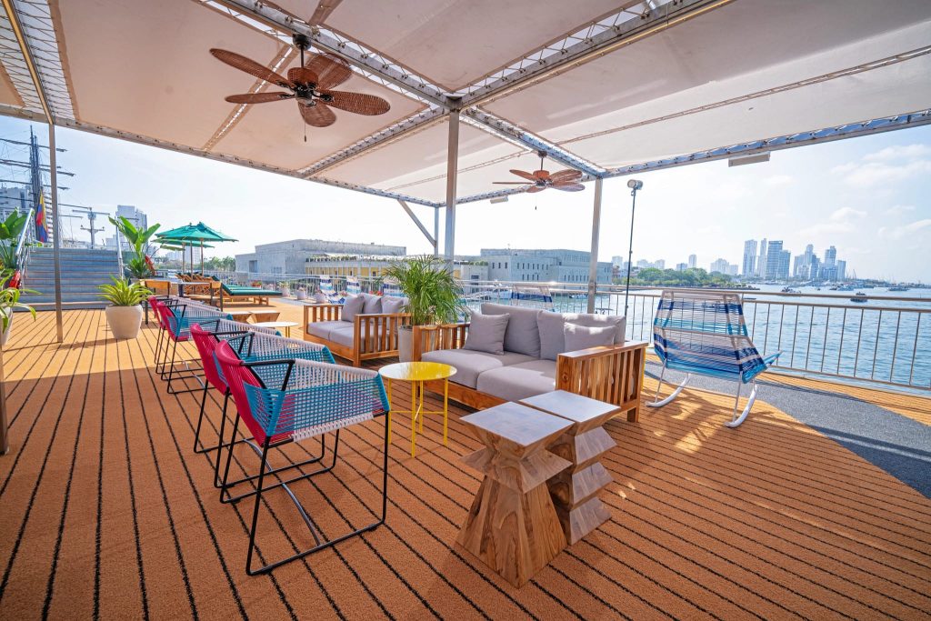 Open upper deck with shaded lounge seating and a rocking chair along the railing above the harbor.