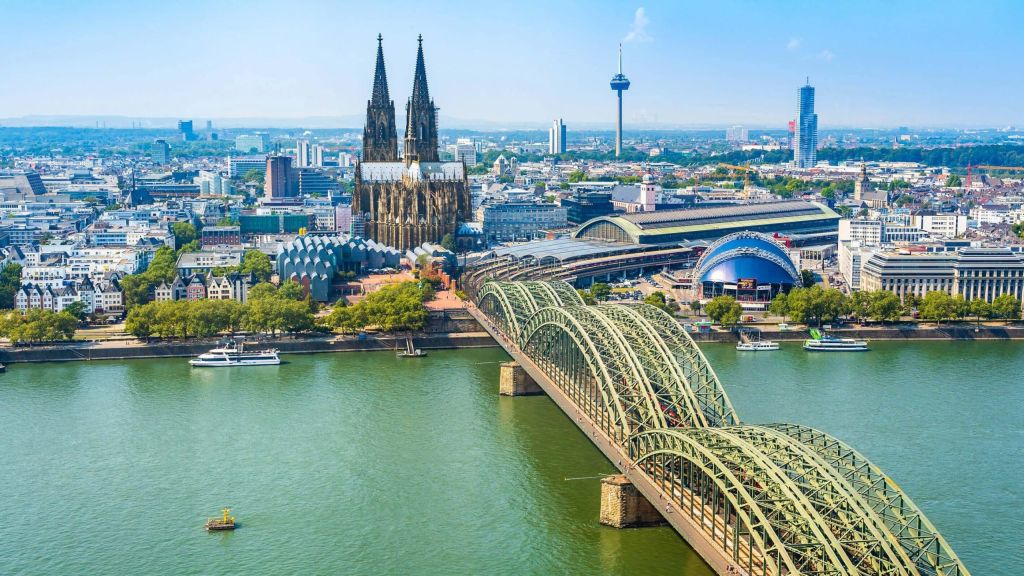 Aerial view of Cologne with twin-spired cathedral, an arched steel bridge over the Rhine and river boats.
