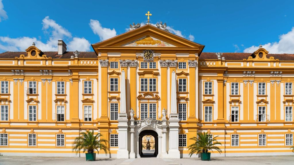 Baroque yellow palace façade with white decorative details, a central arch entrance, and a blue sky.