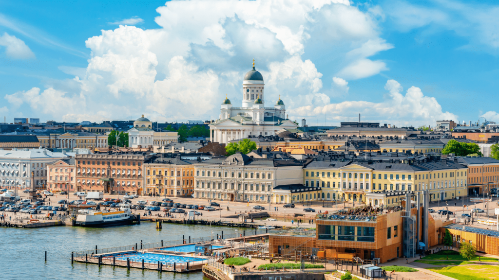 Harborfront cityscape with pastel buildings along the waterfront and a white domed cathedral in the background on a sunny day.