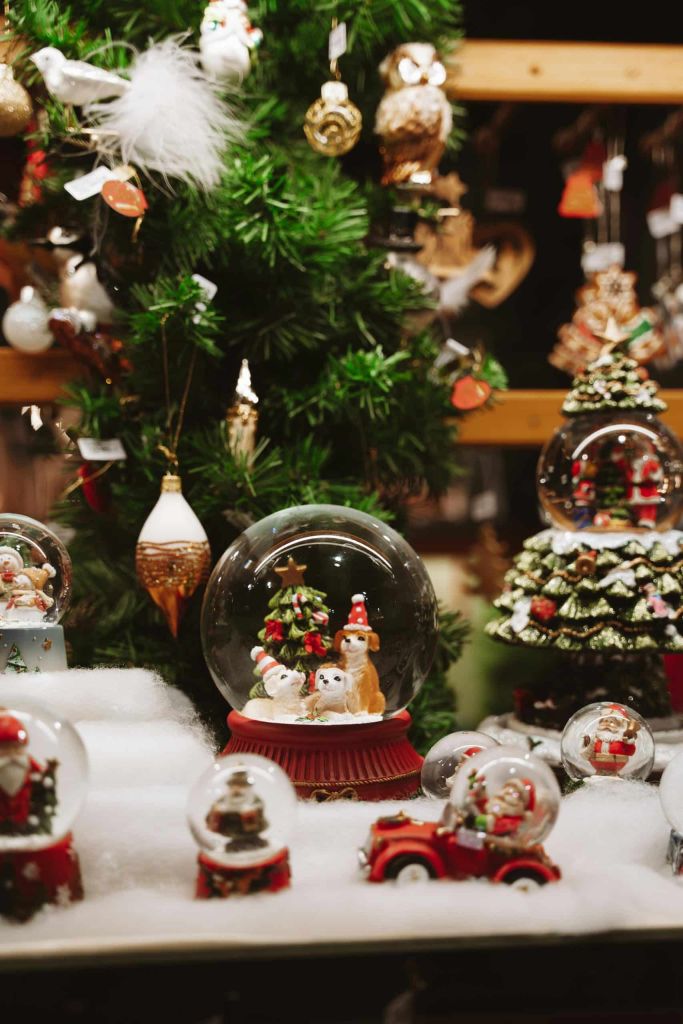 Christmas snow globes and ornaments on display beside a decorated tree in a shop.