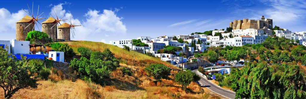 Row of old windmills above a whitewashed hillside town topped by a castle.