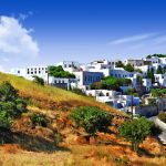Row of old windmills above a whitewashed hillside town topped by a castle.