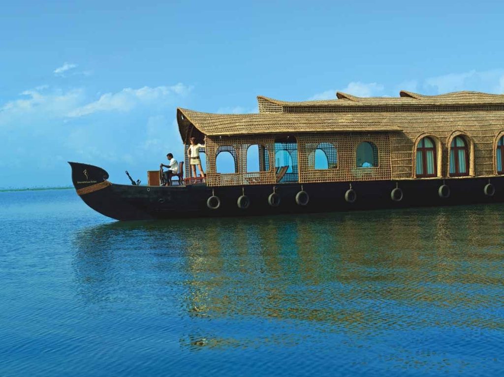 Traditional wooden houseboat with a thatched roof gliding on calm blue backwaters.