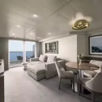 Suite living room with a grey sofa, round marble dining table and a balcony with a sea view.