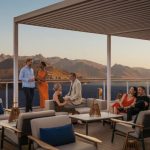 Guests relax on a sunset-lit terrace overlooking mountains and the sea.