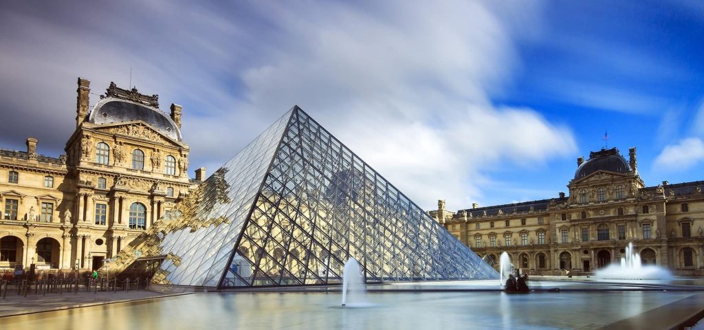 Glass pyramid in a museum courtyard with fountains, flanked by ornate stone palace wings.