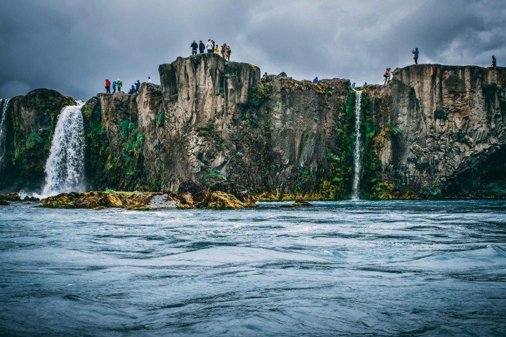 Waterfalls pouring from basalt cliffs with visitors on the clifftop above a churning river.