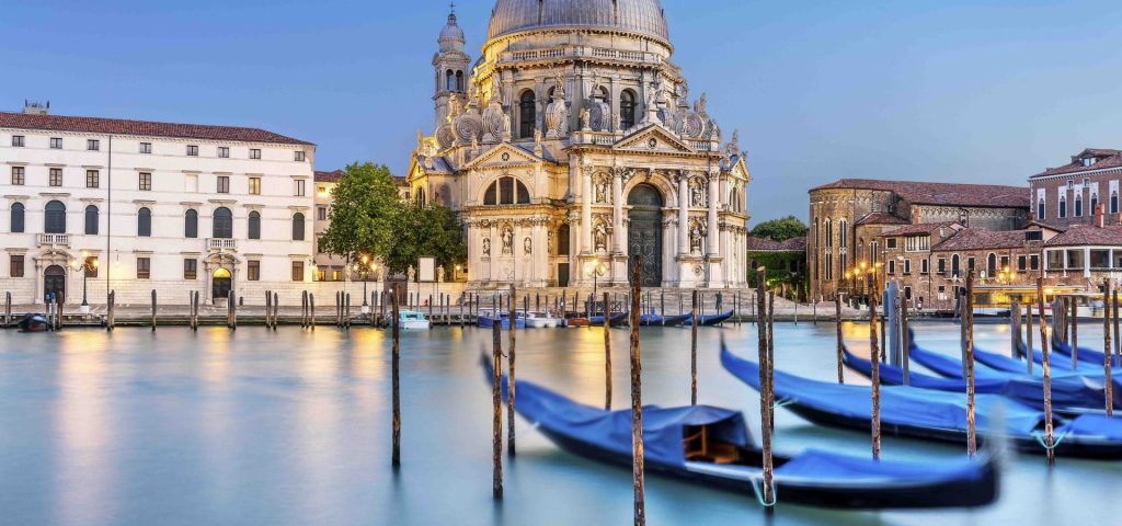 Venice Grand Canal with gondolas moored in front of a domed basilica at dusk.