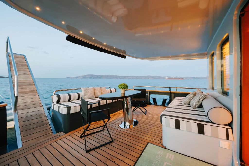 Yacht sun deck with striped seating, a round table and a gangway down to the calm sea.