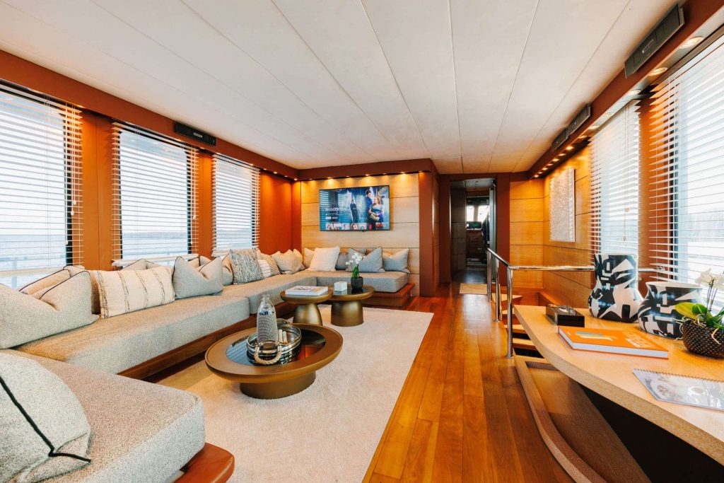Yacht lounge with cream sofas, round coffee tables, wood flooring and window blinds.