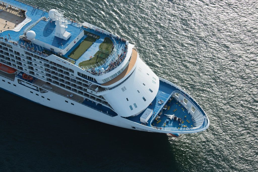 Aerial view of a large white cruise ship's bow and top deck above the sea.