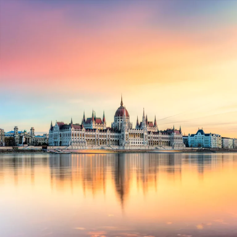 Budapest Parliament Building along the Danube at sunset, reflected in calm water.