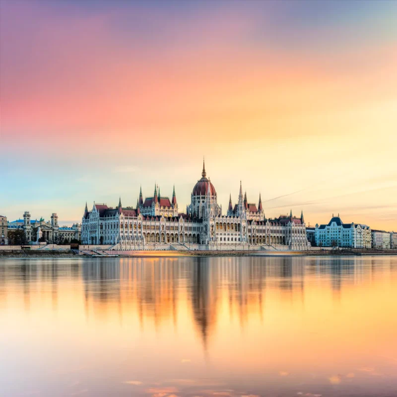 Budapest Parliament Building along the Danube at sunset, reflected in calm water.